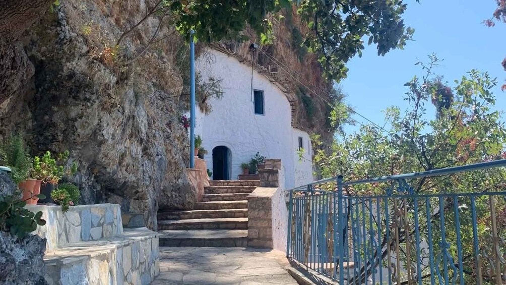 A stone staircase leading to a white building with a small window, surrounded by greenery and a metal railing. 3
