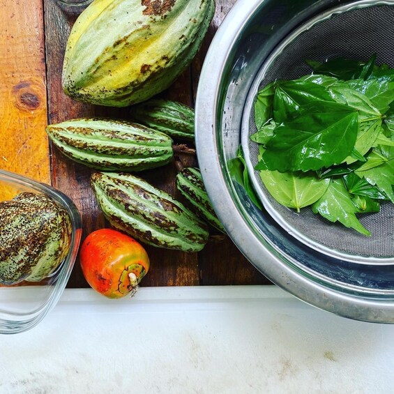 A wooden surface with various gourds, a metal colander with green leaves, and a glass bowl. 1