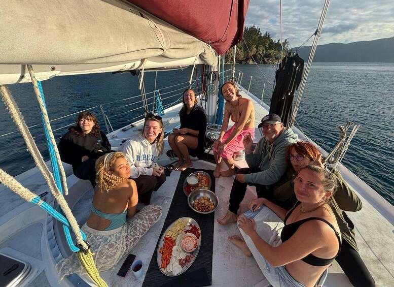 A group of people on a sailboat, gathered around a table with food and drinks. 3