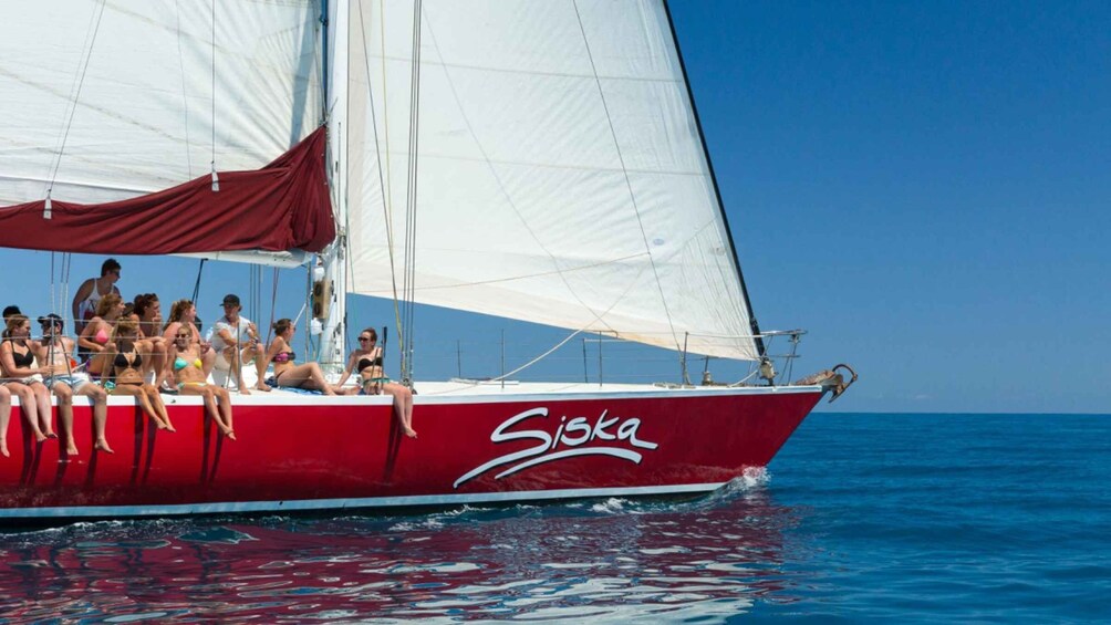 A red sailboat with the name 'Siska' on the side, sailing on blue water. 1