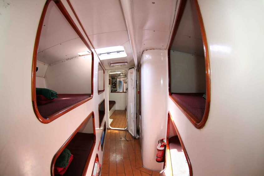 A narrow corridor with bunk beds on either side, a tiled floor, and a fire extinguisher mounted on the wall. 5