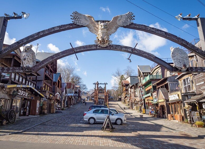 A street with a large archway featuring an eagle sculpture, surrounded by wooden buildings and shops. 4