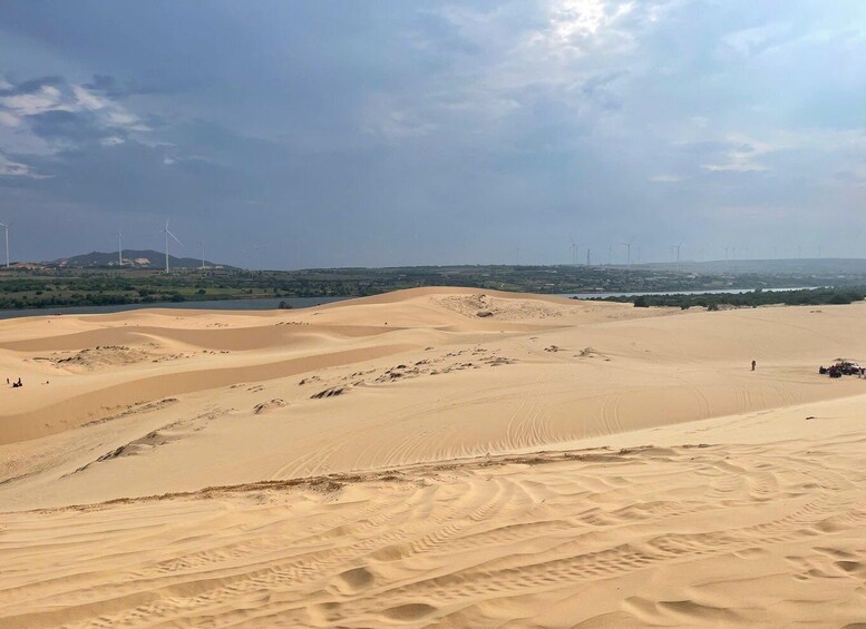 A desert landscape with sand dunes, a clear sky, and wind turbines in the distance. 3