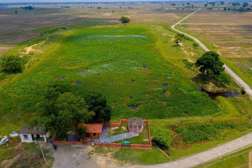 An aerial view of a green field with a pond, a small building, and a dirt road. 2