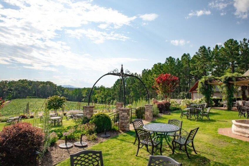 A garden with outdoor seating, a gazebo, and a vineyard in the background. 2