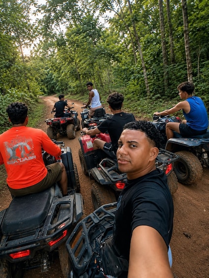 A group of people on ATVs on a dirt path through a forest. 1
