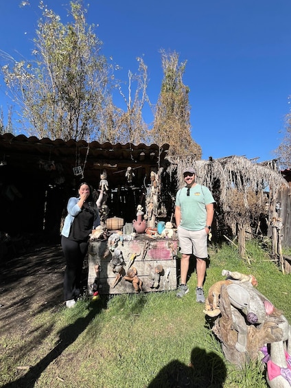 A rustic outdoor setting with a wooden structure, various sculptures, and a clear blue sky. 2
