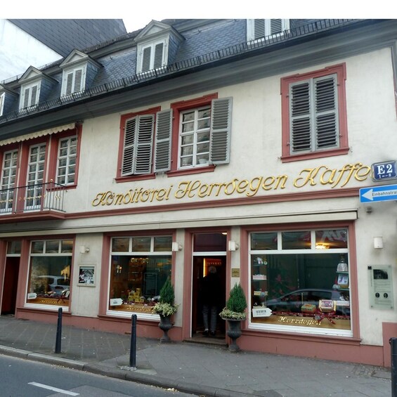A building with the sign 'Konditorei Herrdegen Kaffe' and a street sign indicating 'E2'. 4