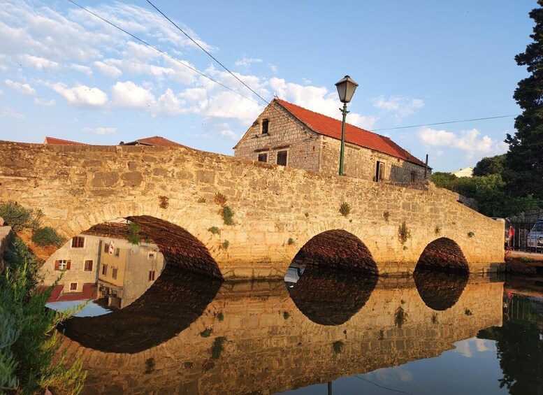 A stone bridge with three arches over a body of water, reflecting the bridge and surrounding buildings. 3