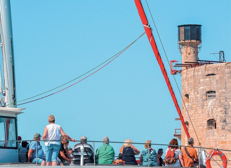 A group of people on a boat, a red crane, and a historic stone tower. 2