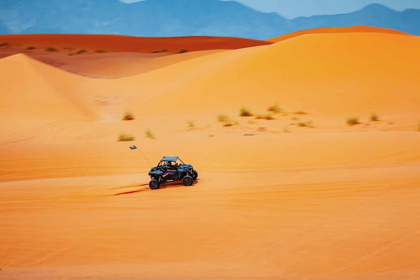 A remote desert landscape with sand dunes and a single off-road vehicle. 3