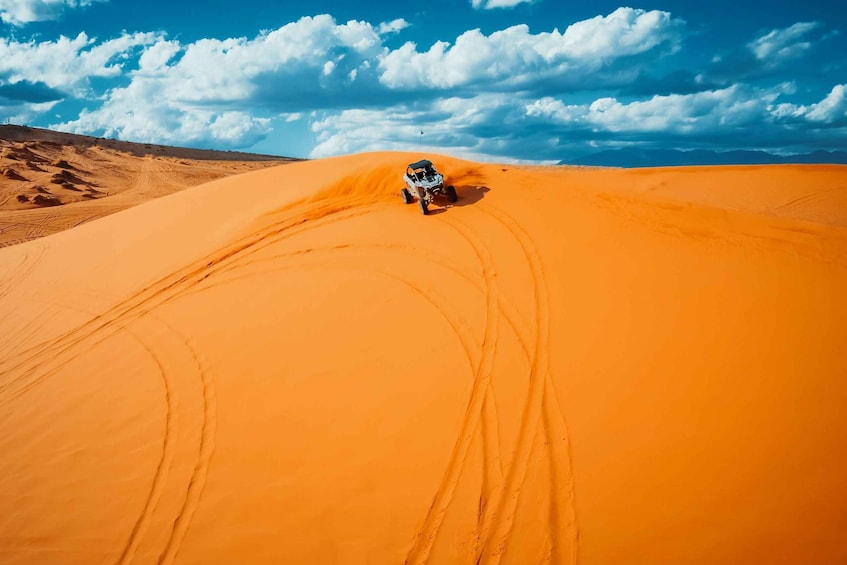 A vehicle driving on a sandy dune with a clear blue sky and clouds in the background. 5