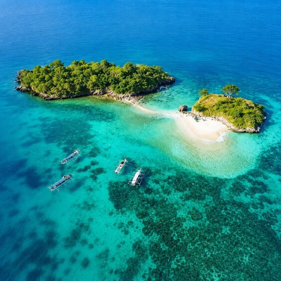 An aerial view of a tropical island with clear turquoise waters, a sandy beach, and several traditional boats anchored near the shore. 3