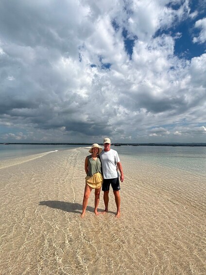A couple standing on a beach with clear water and a cloudy sky. 4
