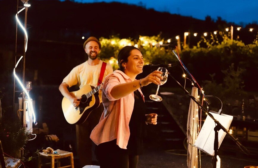 Two people performing music outdoors at night with string lights and a guitar. 2