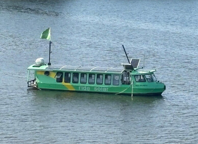 A green boat with solar panels and a flag on a body of water. 5