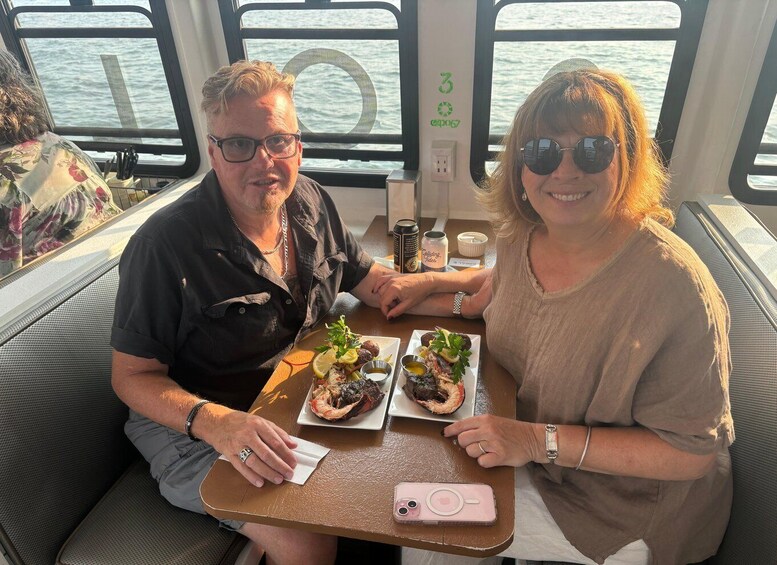 Two people seated at a table with food and drinks on a boat. 3