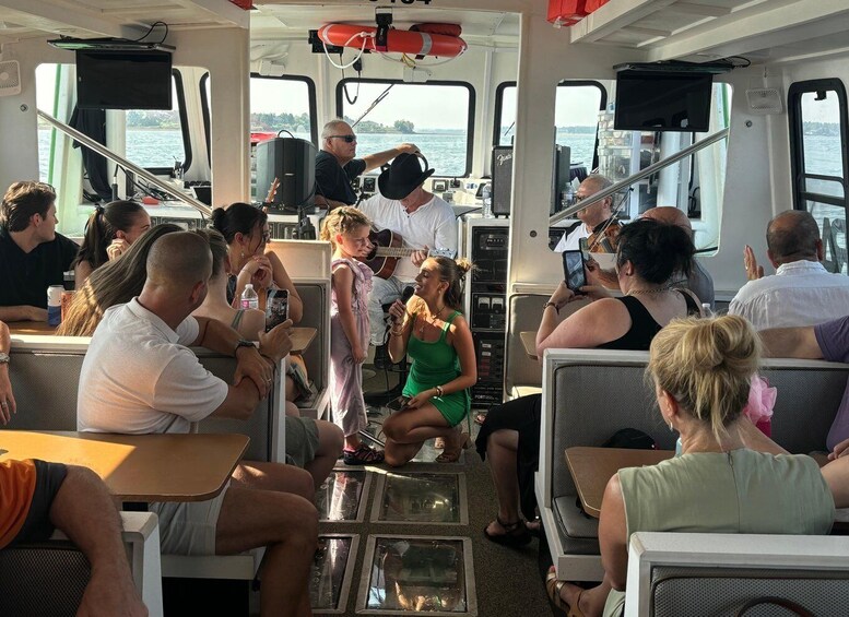 A group of people on a boat, some seated, some standing, with a man playing a guitar. 1