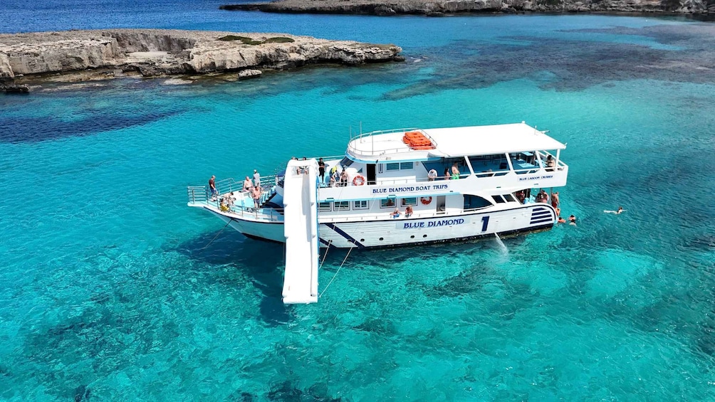 A boat named 'Blue Lagoon Cruises' with passengers on board, floating in clear turquoise waters near rocky formations. 1