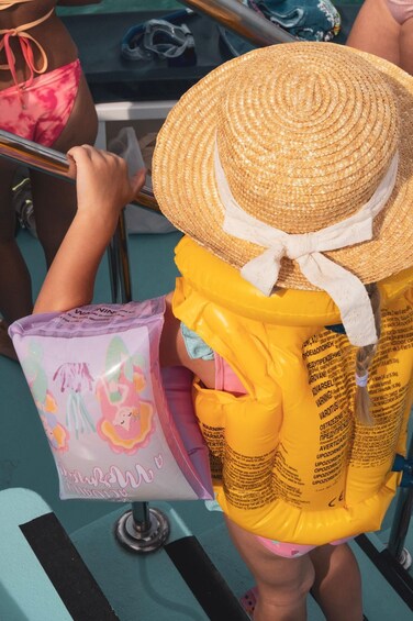 A person wearing a straw hat and a yellow swimsuit with a white ribbon, holding a purple bag with a unicorn design. 4