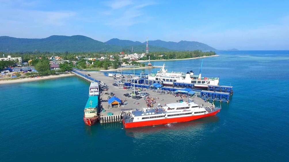 A ferry dock with a large red and white ferry, a pier, and a beach with buildings in the background. 3
