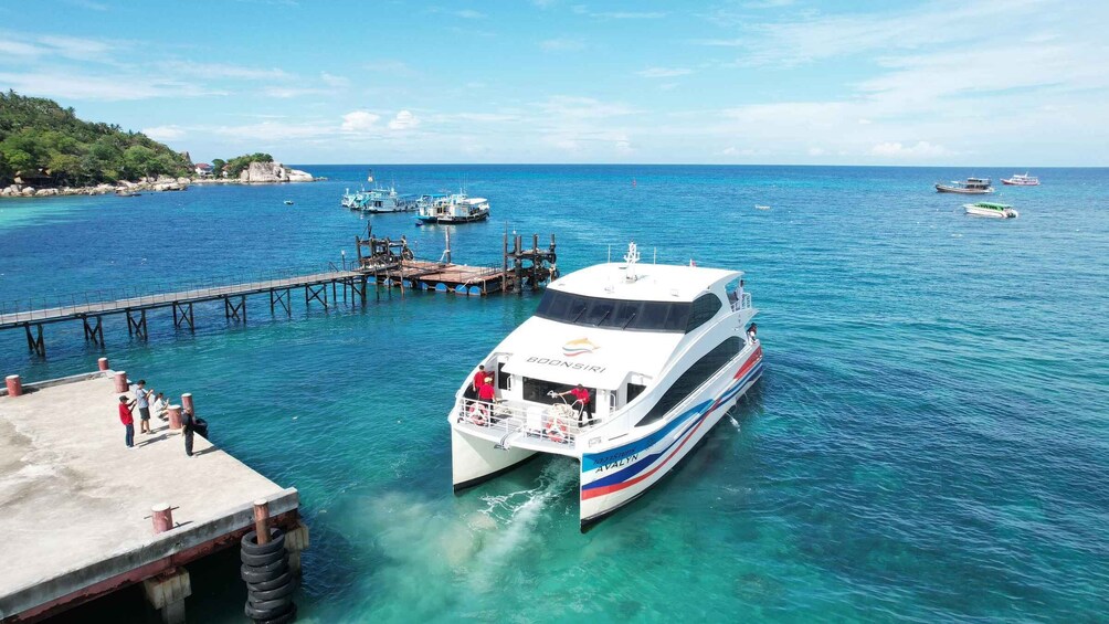 A white boat docked at a pier with clear blue water and a few other boats in the background. 3