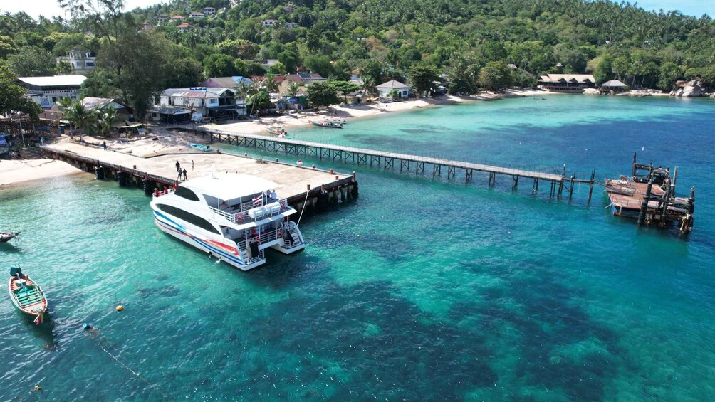 A coastal area with a pier extending into turquoise waters, a boat docked at the pier, and a small boat near the shore. 2