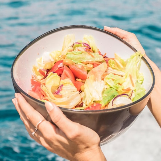 A bowl of salad with various vegetables held by hands against a water background. 3