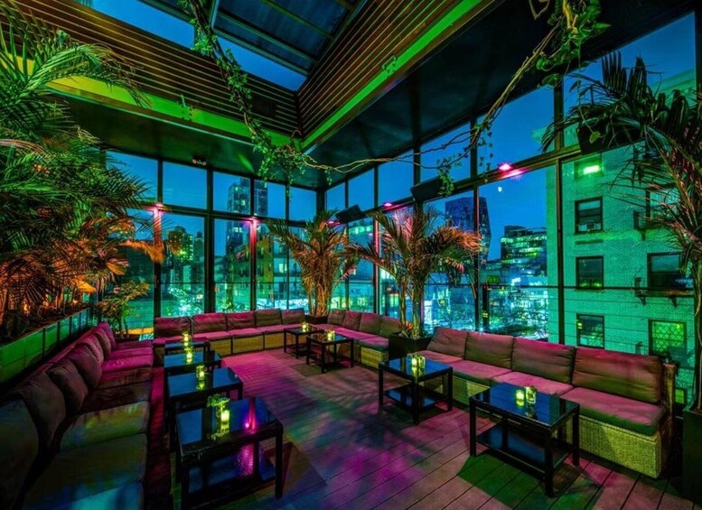 An indoor lounge with a city view, featuring a wooden ceiling, green ambient lighting, and a variety of seating arrangements. 2