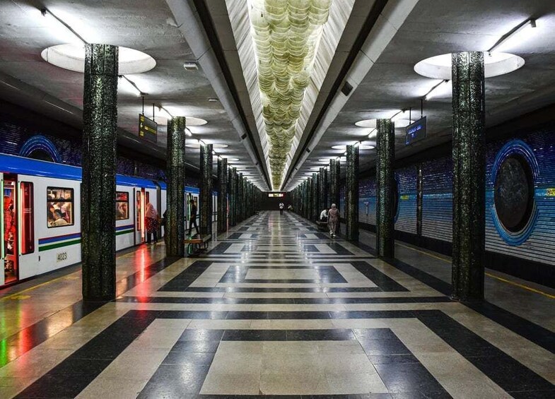 A subway station with a central walkway, train tracks, and a train on the left. 1