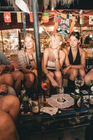 A group of people sitting at a table with drinks and playing cards. 5