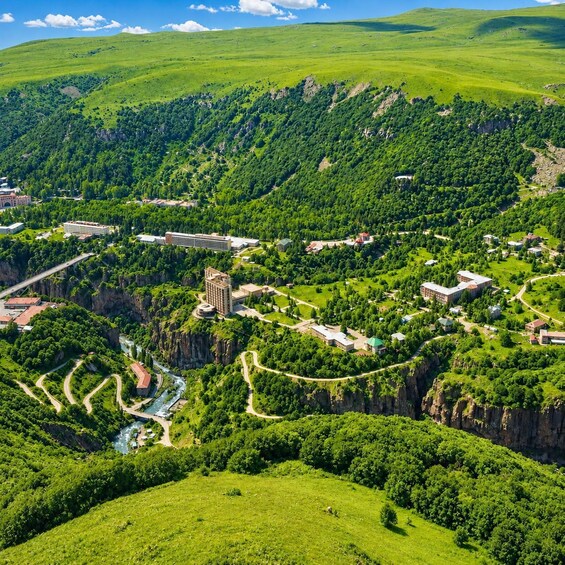 A lush green landscape with a river, buildings, and a bridge. 1