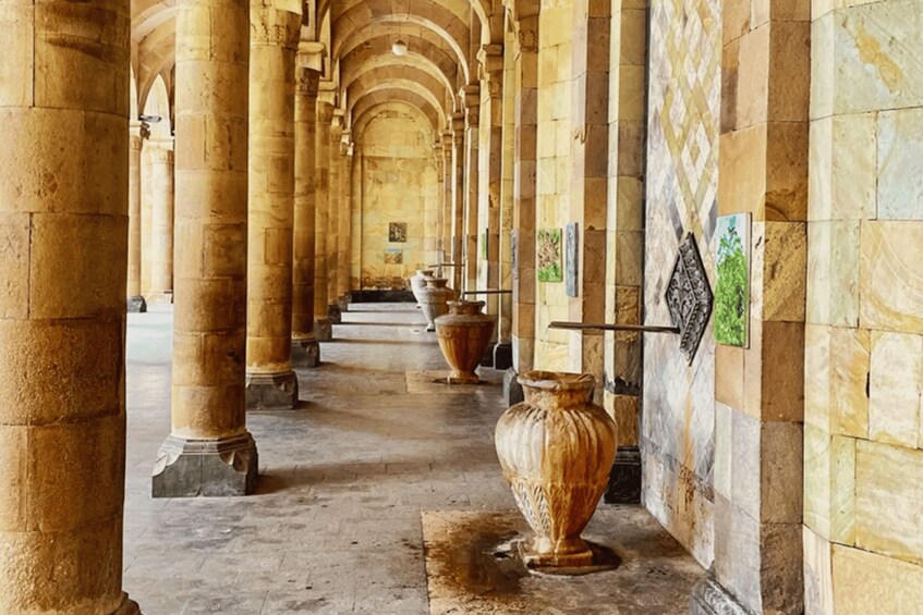 A corridor with columns, a large vase, and tiled walls. 2