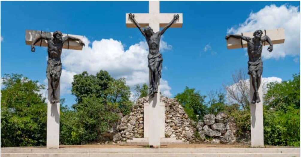 Three crucifix statues in a row with a stone pile and trees in the background. 2