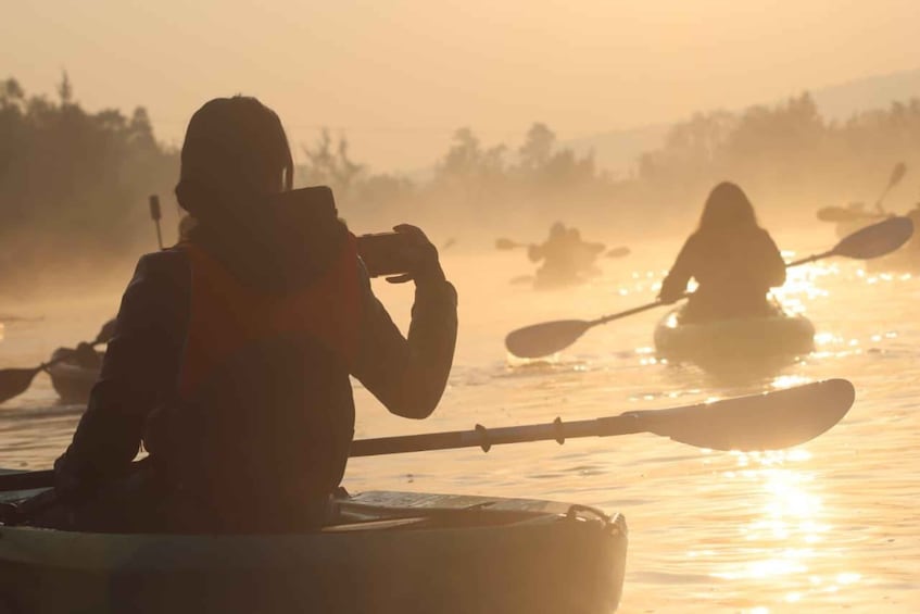 A person kayaking on a river during sunrise or sunset. 1