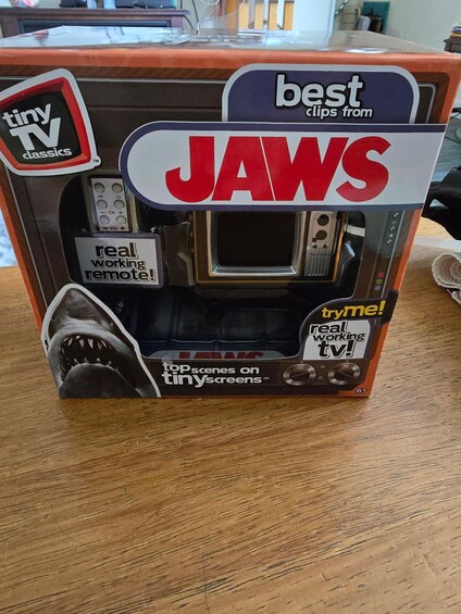 A toy TV set in a box labeled 'Jaws' with 'real working remote' and 'tryme!' text. 4