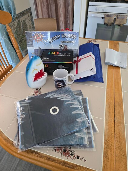 A table with a 3D visualization lamp, a mug, a shark toy, and a welcome sign for Amity Island. 3