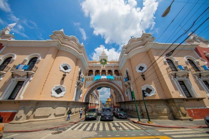 A street with a large archway, buildings with balconies, and a clear blue sky. 2