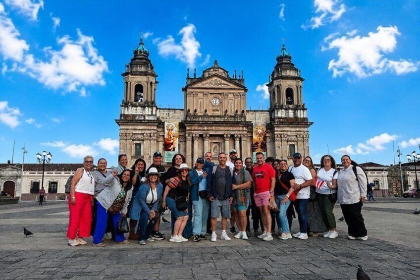 A group of people posing in front of a historic building with two bell towers and a central facade. 1