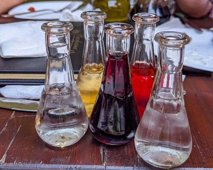Five glass bottles with different colored liquids on a wooden surface. 4