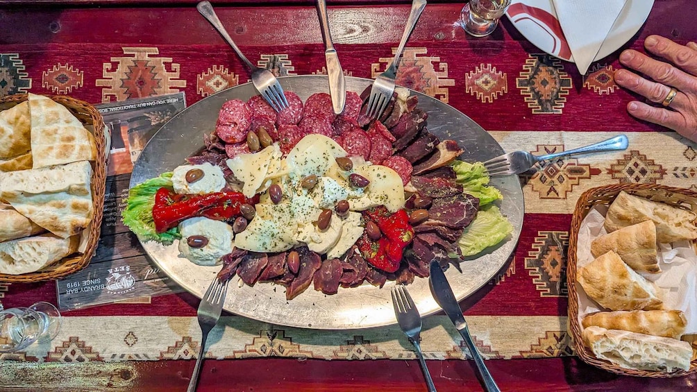 A platter of assorted meats, cheeses, and olives on a table with a patterned tablecloth. 3