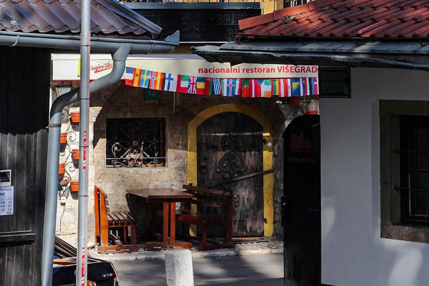 A street scene with a restaurant named 'nacionalni restoran Visegrad' and a variety of flags hanging above the entrance. 5