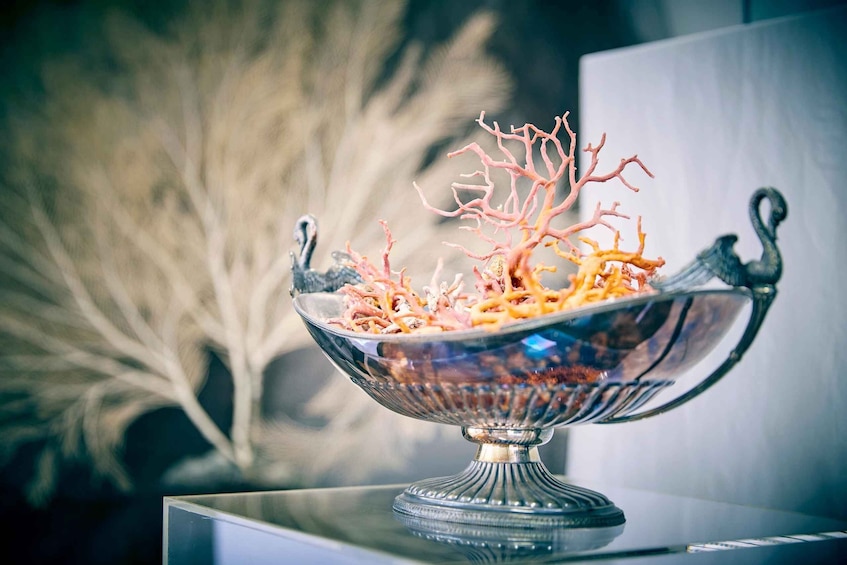 A decorative glass bowl with a swan design, filled with colorful branches, placed on a reflective surface. 2