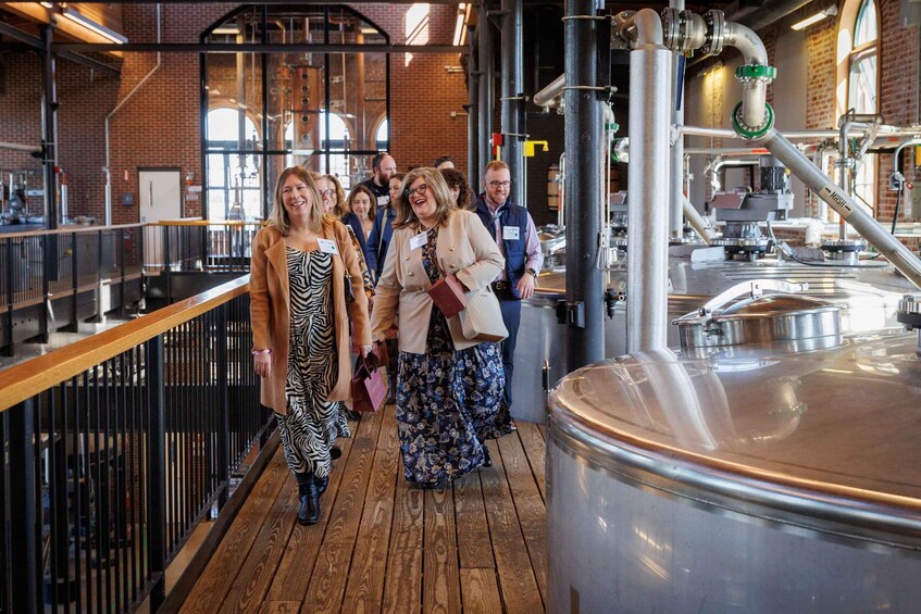 A group of people in a brewery with large stainless steel tanks and wooden flooring. 5