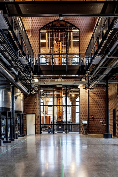 A spacious industrial interior with exposed brick walls, large metal tanks, and a mezzanine level with a staircase. 3