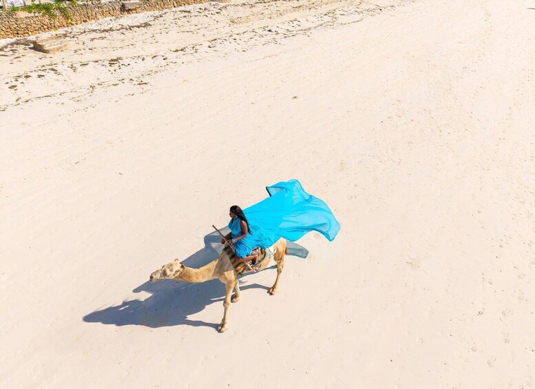 A person riding a camel on a sandy terrain with sparse vegetation. 4