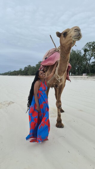 A person standing next to a camel on a sandy beach with trees in the background. 5
