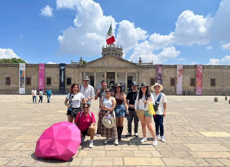 A group of people standing in front of a historical building with a flag. 1