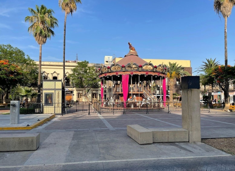 A carousel with pink curtains, palm trees, and a building in the background. 4