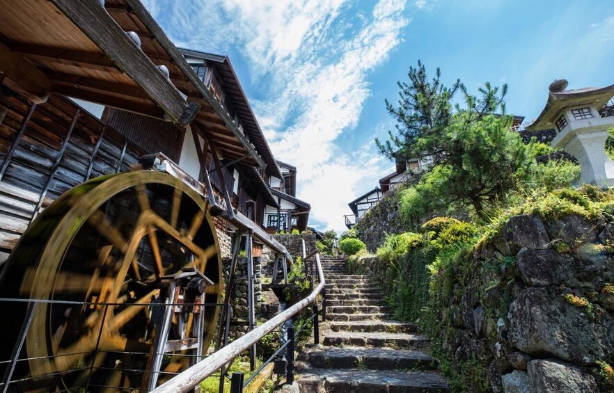 A wooden staircase leading up to a traditional building with a large water wheel. 3